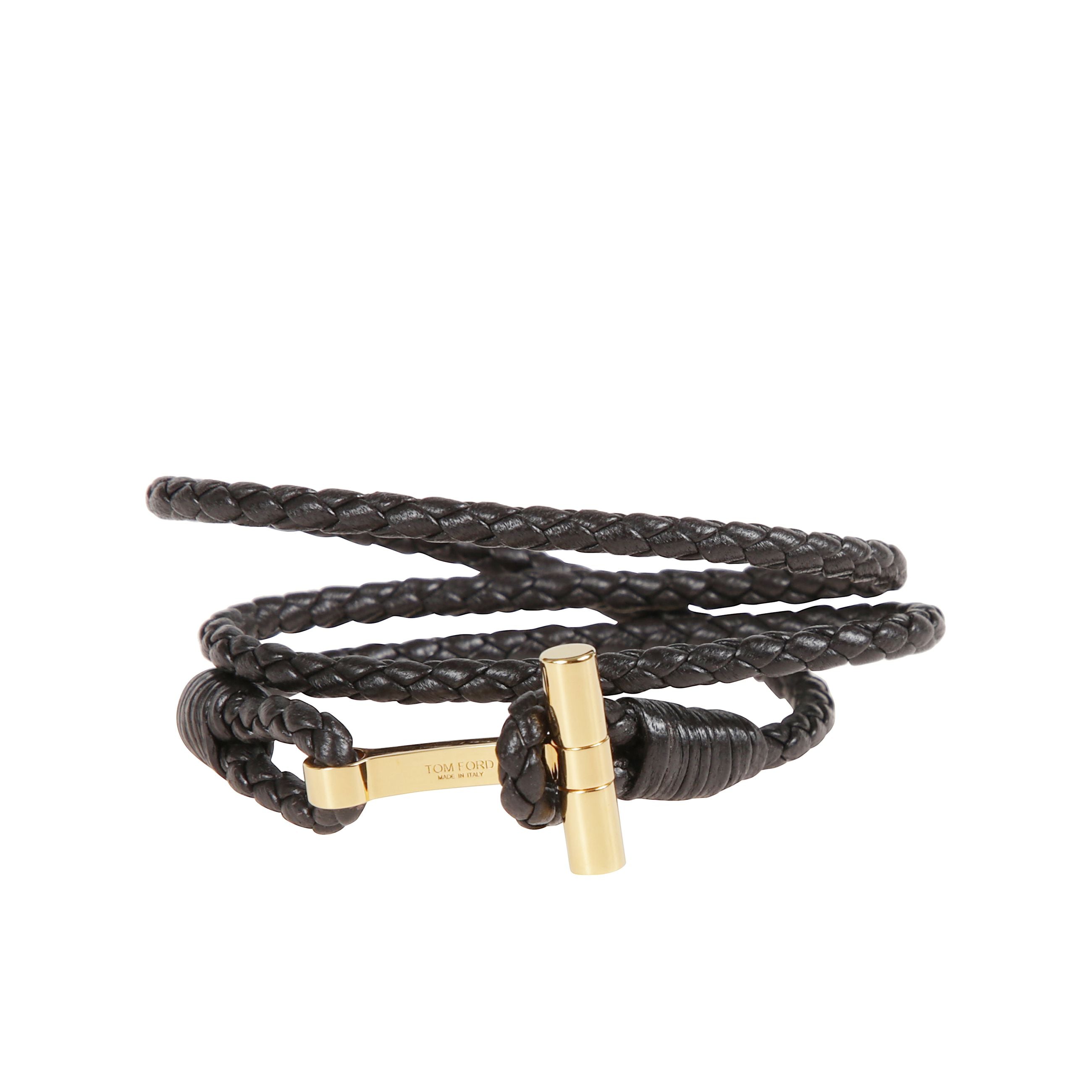 Bracciale in pelle a fascia intrecciata. chiusura ad alamaro con placca in bronzo dorato che riporta il simbolo tom ford.